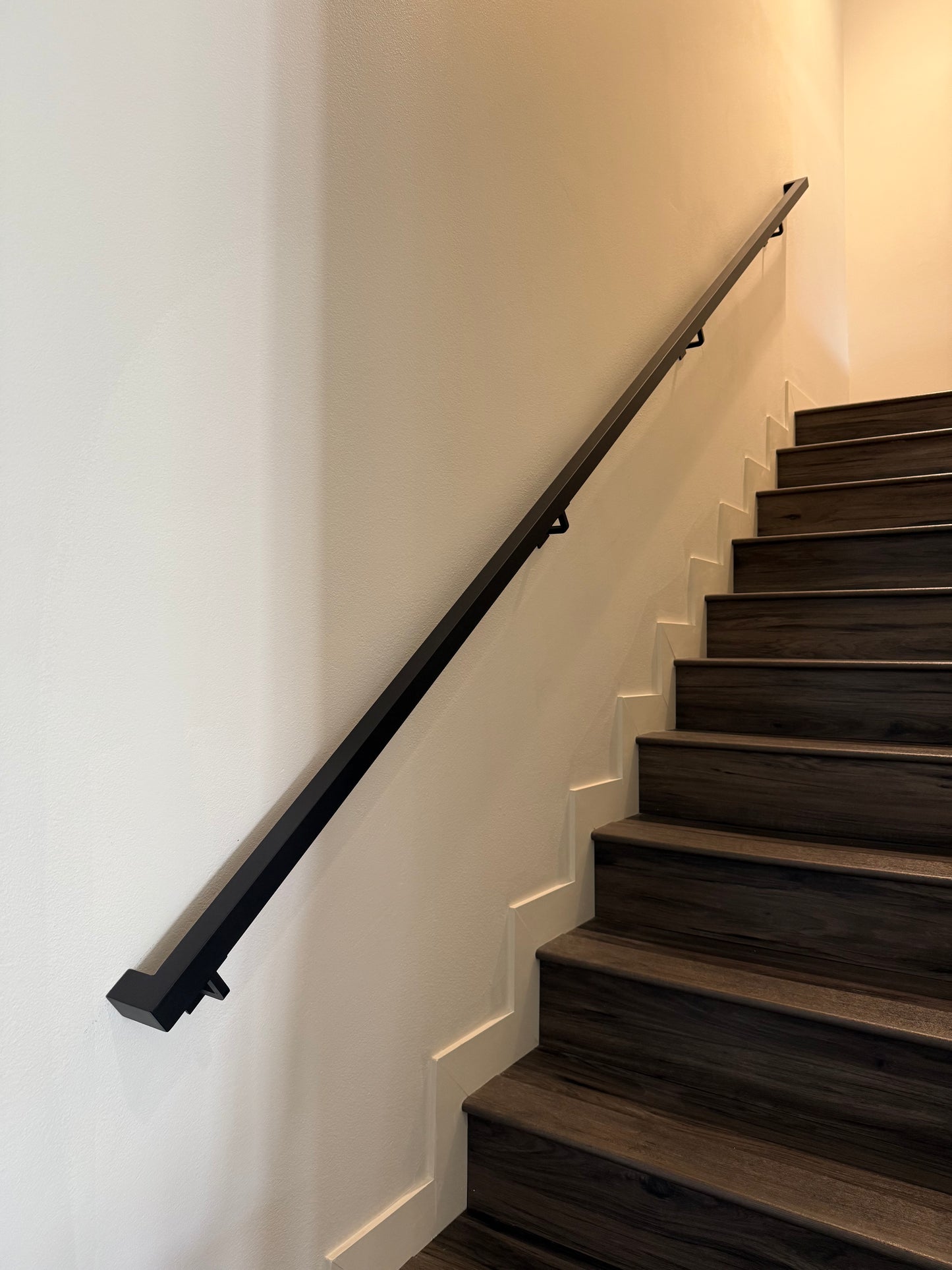 view from the bottom of a flight of 12 stairs looking upwards at the 1.5"x1.5" Metal Handrail running from the bottom to the top of the stairs