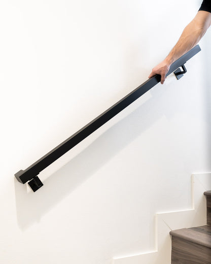 person's hand grabbing onto the 1.5"x1.5" Metal Wall Handrail to walk down the stairs