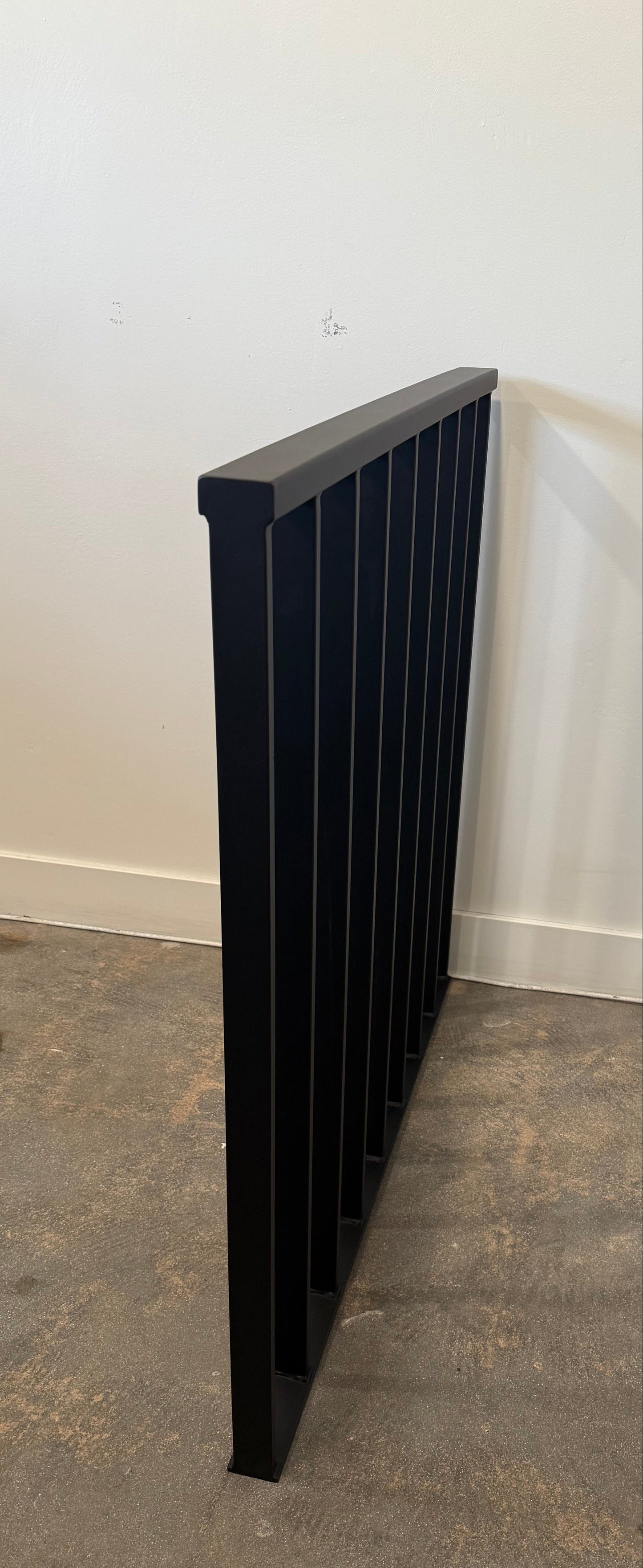 Black metal rail against a white wall and concrete floor.