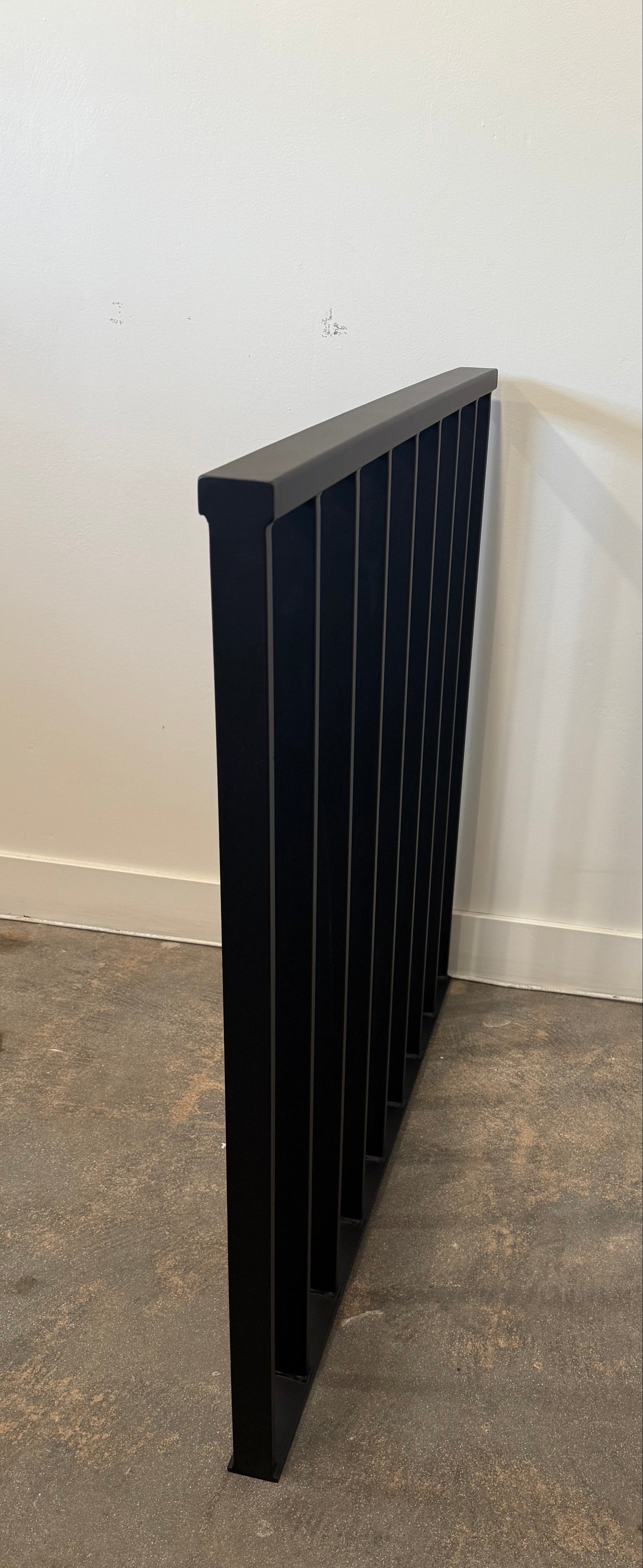 Black metal rail against a white wall and concrete floor.