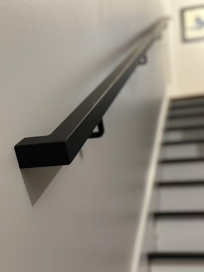 close view of the 1.5"x1.5" Metal Handrail on light grey wall above steps with black tread and white risers